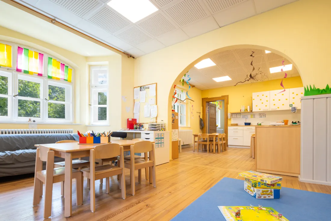 Großer, bunter Gruppenraum vom Kindergarten mit Brettspielen, Tischen und Stühlen mit Stiften zum Malen